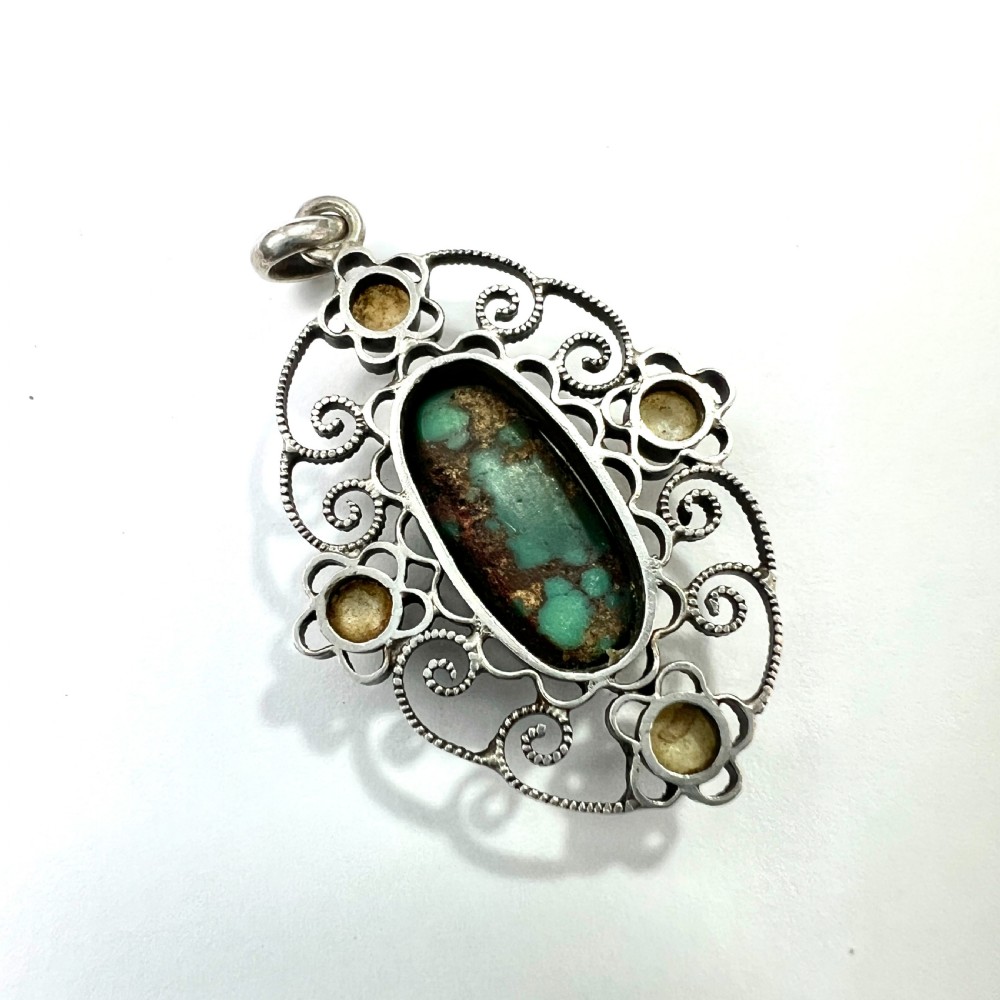 An oval silver pendant featuring an openwork scrollwork design set with a central green turquoise matrix cabochon and four small pearl accents. View IV