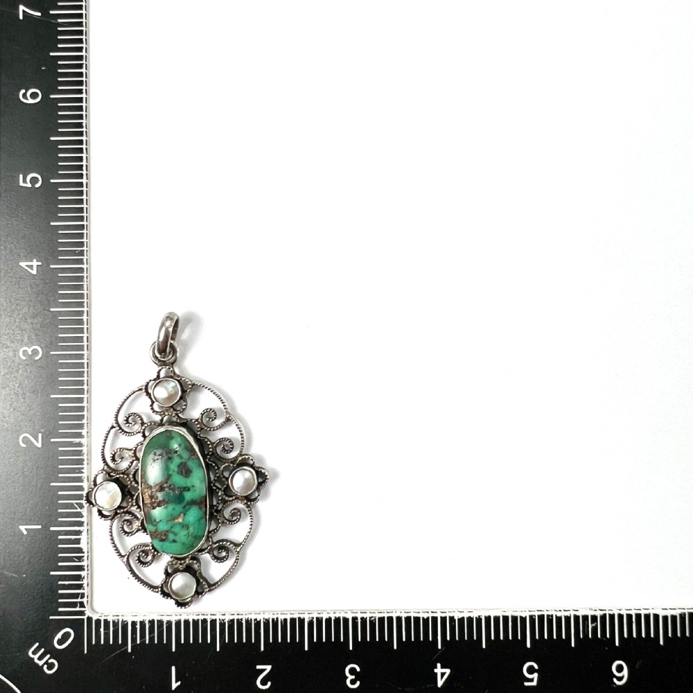 An oval silver pendant featuring an openwork scrollwork design set with a central green turquoise matrix cabochon and four small pearl accents. View V