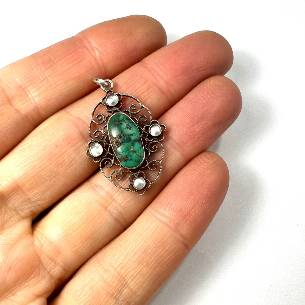 An oval silver pendant featuring an openwork scrollwork design set with a central green turquoise matrix cabochon and four small pearl accents. View VI
