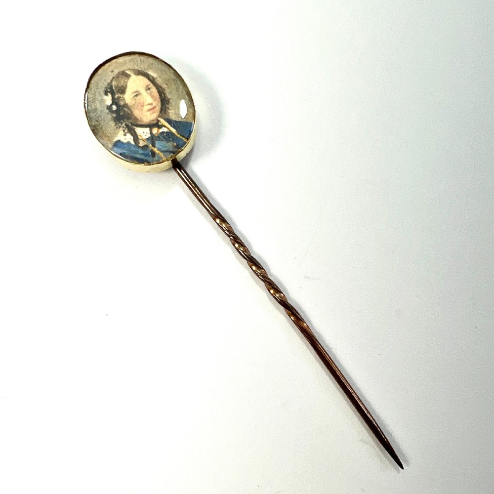 An antique gold stick pin featuring an oval miniature portrait painting of a lady in a blue dress with dark curls. View II