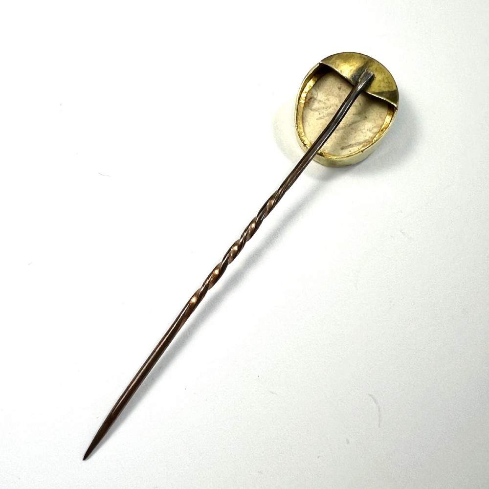 An antique gold stick pin featuring an oval miniature portrait painting of a lady in a blue dress with dark curls. View IV