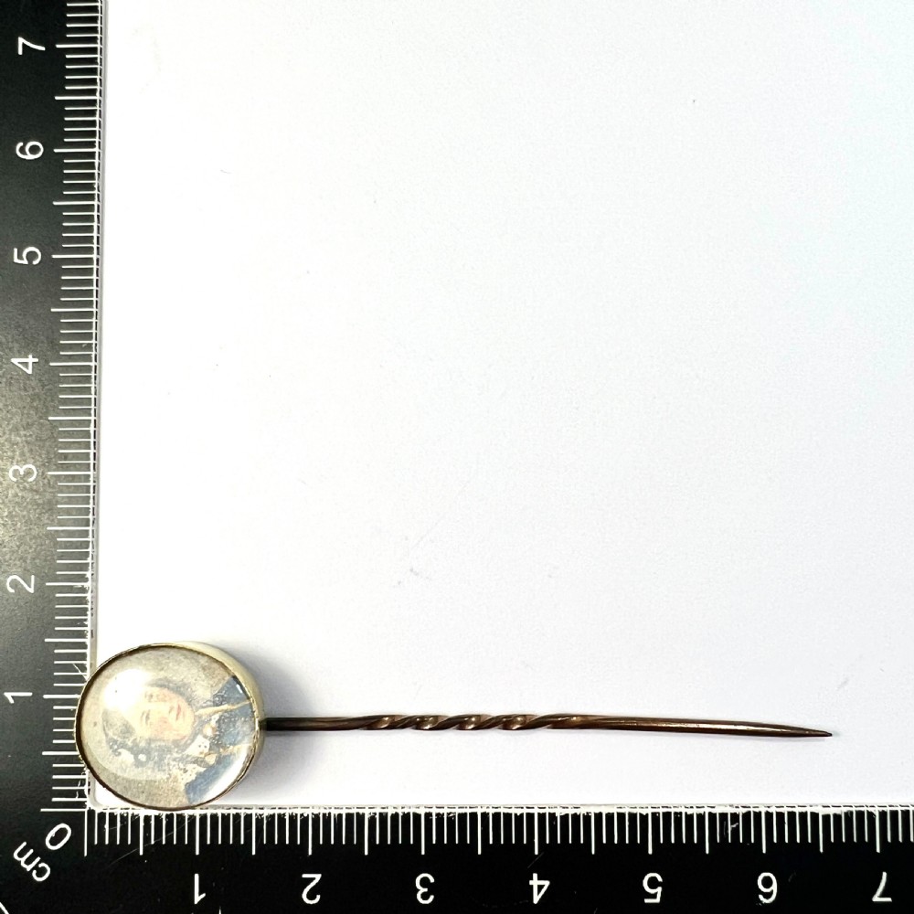 An antique gold stick pin featuring an oval miniature portrait painting of a lady in a blue dress with dark curls. View VI