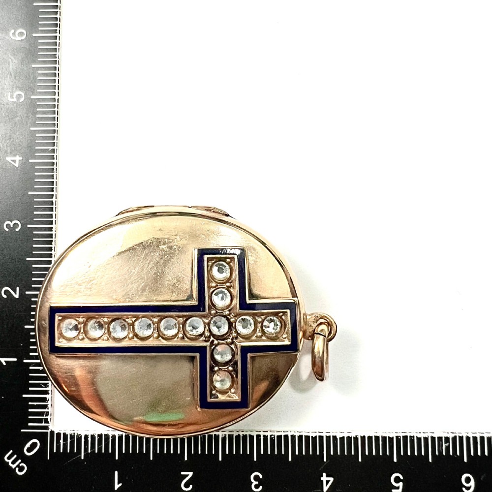 An oval rolled gold Victorian locket featuring a central blue enamelled cross set with round paste stones. View VII