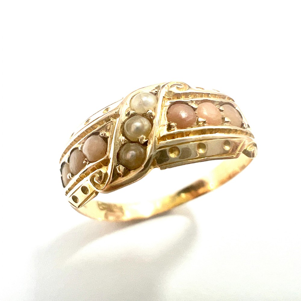 A Victorian 15 carat gold band ring set with rows of rounded seed pearls and pink coral cabochons featuring carved side scrollwork.