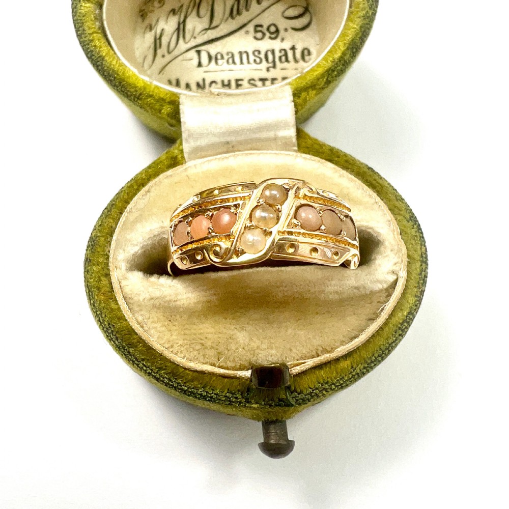 A Victorian 15 carat gold band ring set with rows of rounded seed pearls and pink coral cabochons featuring carved side scrollwork. View VI