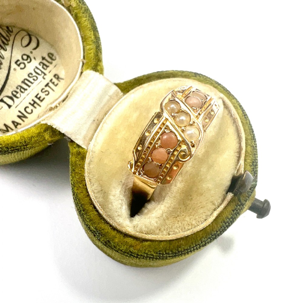 A Victorian 15 carat gold band ring set with rows of rounded seed pearls and pink coral cabochons featuring carved side scrollwork. View VII