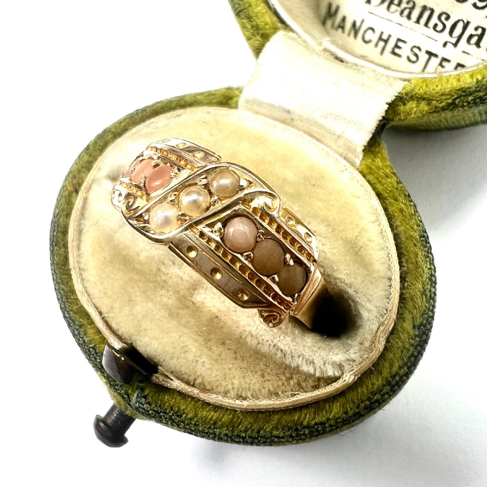 A Victorian 15 carat gold band ring set with rows of rounded seed pearls and pink coral cabochons featuring carved side scrollwork. View VIII
