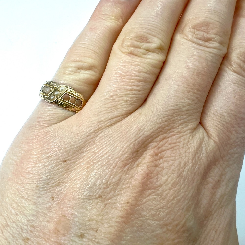 A Victorian 15 carat gold band ring set with rows of rounded seed pearls and pink coral cabochons featuring carved side scrollwork. View IX
