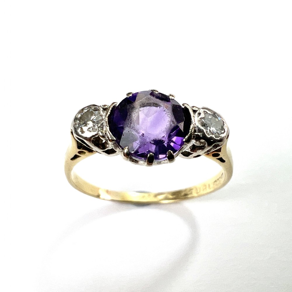 An antique 18ct yellow gold ring featuring a round purple central amethyst flanked by two diamonds in platinum settings.