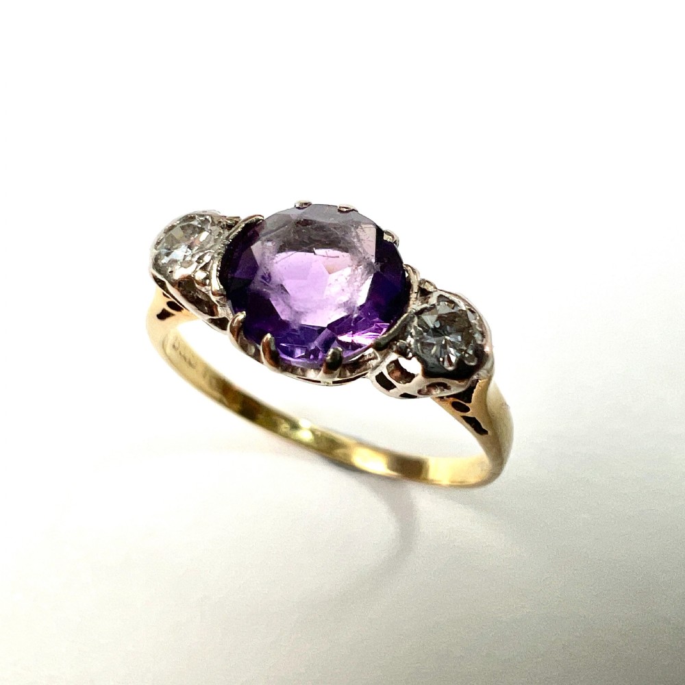 An antique 18ct yellow gold ring featuring a round purple central amethyst flanked by two diamonds in platinum settings. View III