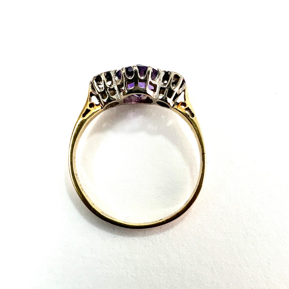 An antique 18ct yellow gold ring featuring a round purple central amethyst flanked by two diamonds in platinum settings. View VI