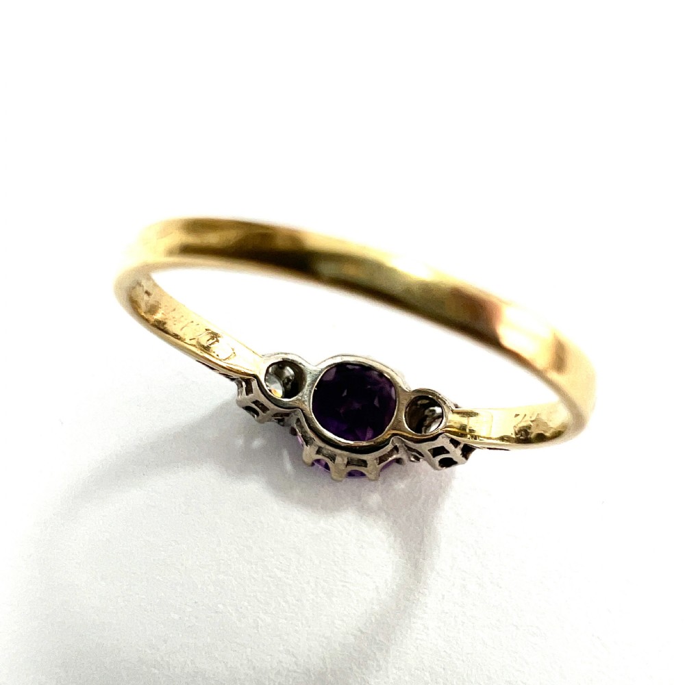 An antique 18ct yellow gold ring featuring a round purple central amethyst flanked by two diamonds in platinum settings. View VII