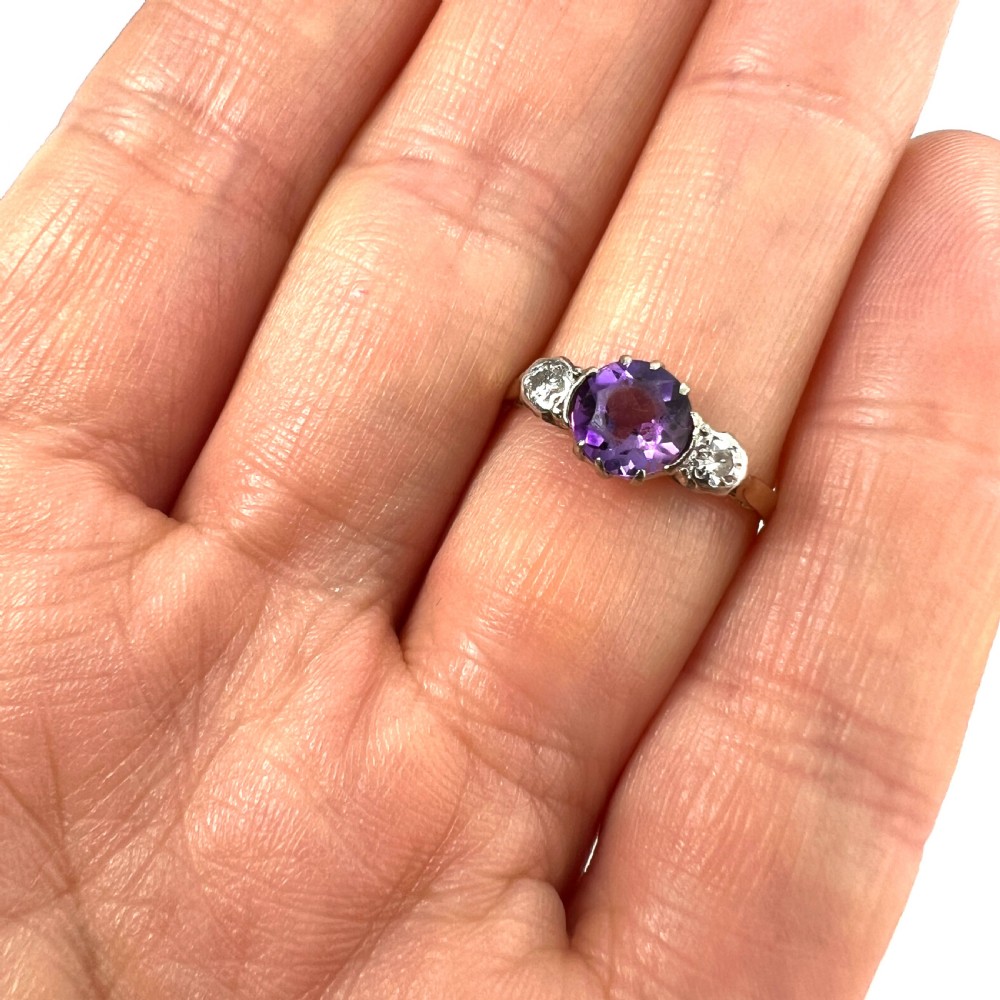 An antique 18ct yellow gold ring featuring a round purple central amethyst flanked by two diamonds in platinum settings. View IX