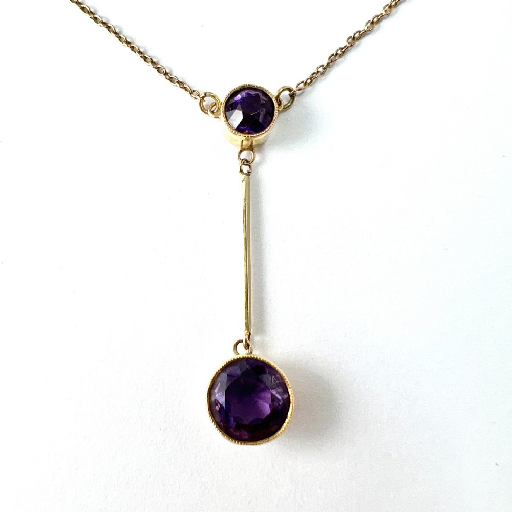 An Edwardian gold drop necklace featuring two round bezel-set purple amethyst stones connected by a slender gold bar on a fine chain. View II
