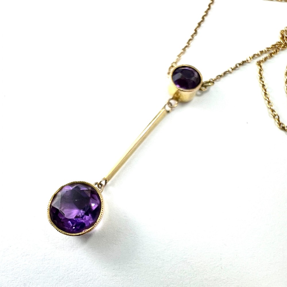An Edwardian gold drop necklace featuring two round bezel-set purple amethyst stones connected by a slender gold bar on a fine chain. View III