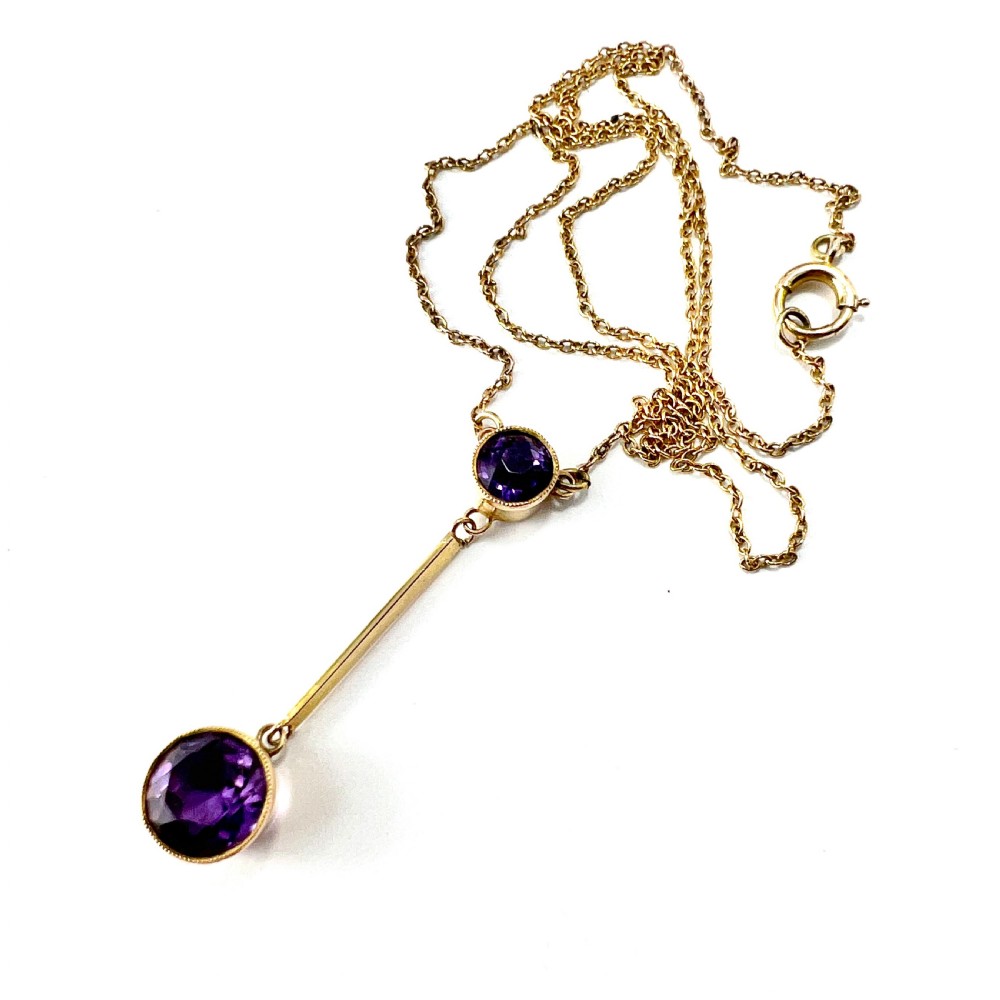 An Edwardian gold drop necklace featuring two round bezel-set purple amethyst stones connected by a slender gold bar on a fine chain. View V