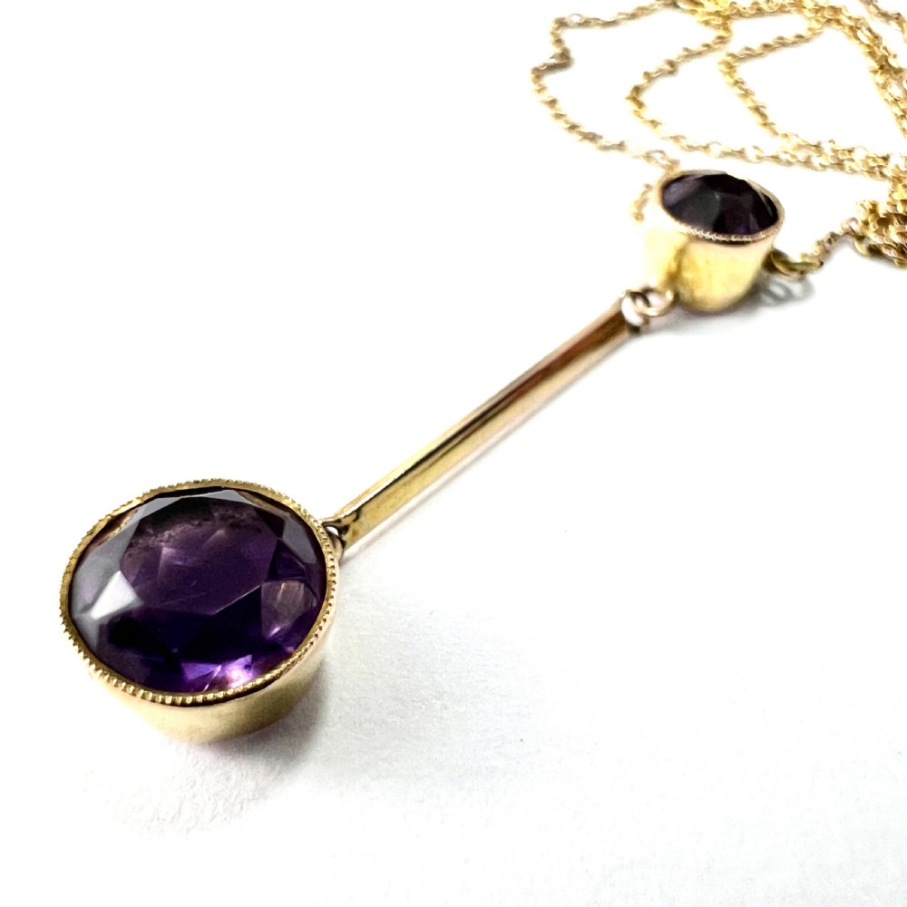 An Edwardian gold drop necklace featuring two round bezel-set purple amethyst stones connected by a slender gold bar on a fine chain. View VI