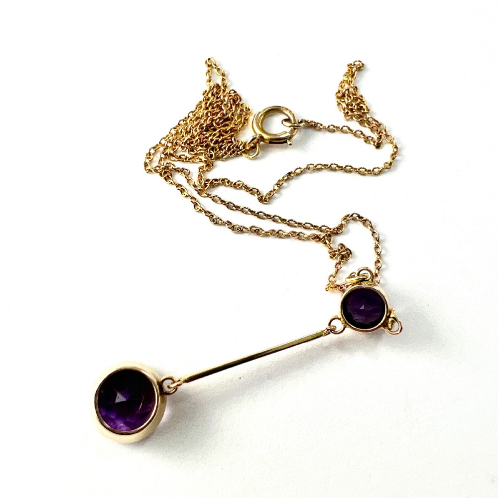 An Edwardian gold drop necklace featuring two round bezel-set purple amethyst stones connected by a slender gold bar on a fine chain. View VII
