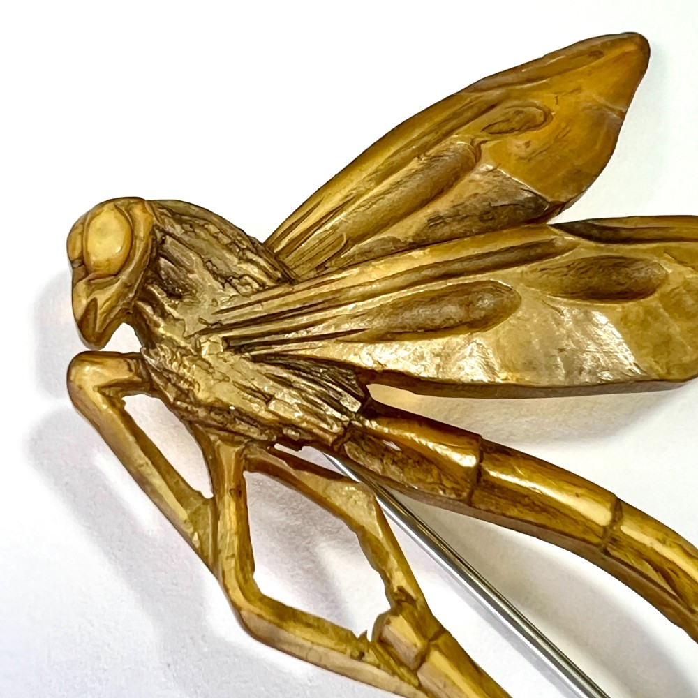 A carved horn brooch in the shape of a dragonfly with detailed wings and a curved body against a neutral background. View II