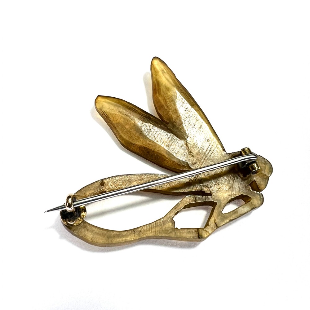 A carved horn brooch in the shape of a dragonfly with detailed wings and a curved body against a neutral background. View III