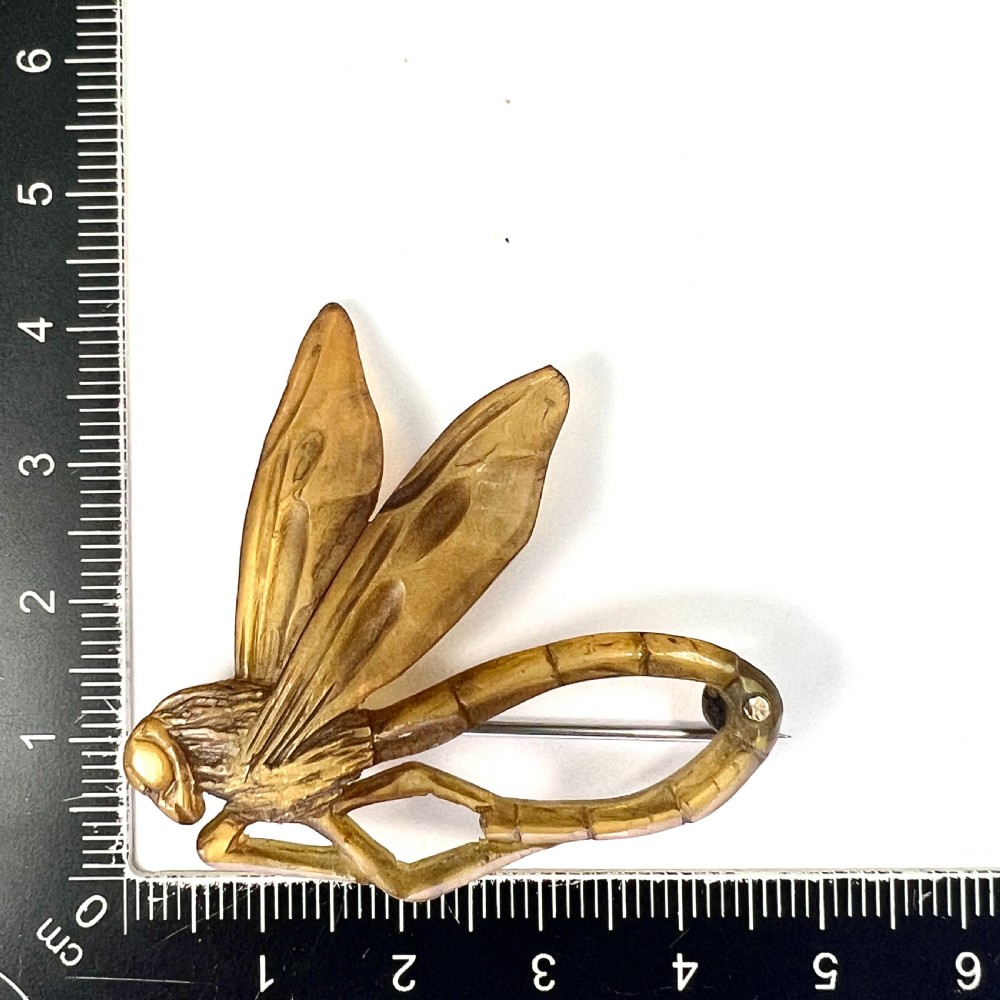 A carved horn brooch in the shape of a dragonfly with detailed wings and a curved body against a neutral background. View V