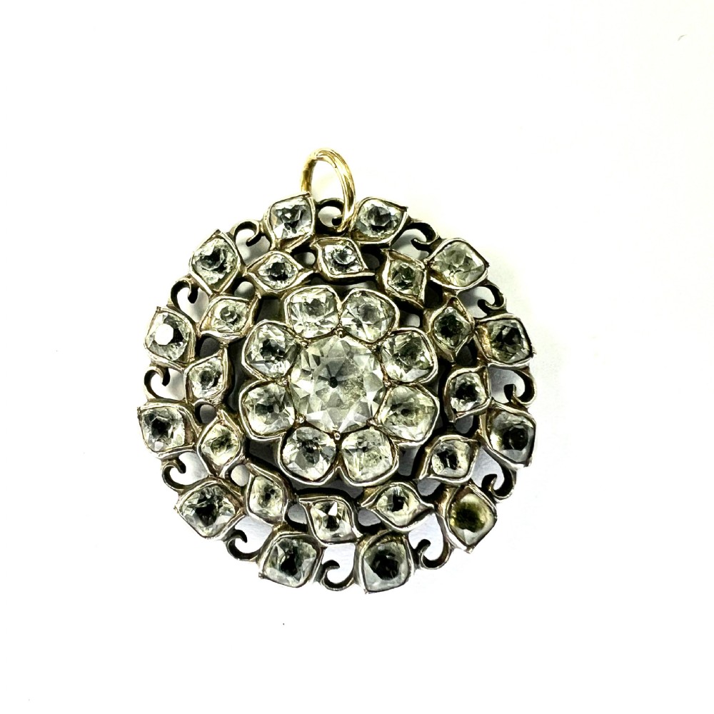A circular Georgian silver pendant featuring faceted clear paste glass stones with black dot culets arranged in a floral cluster pattern.