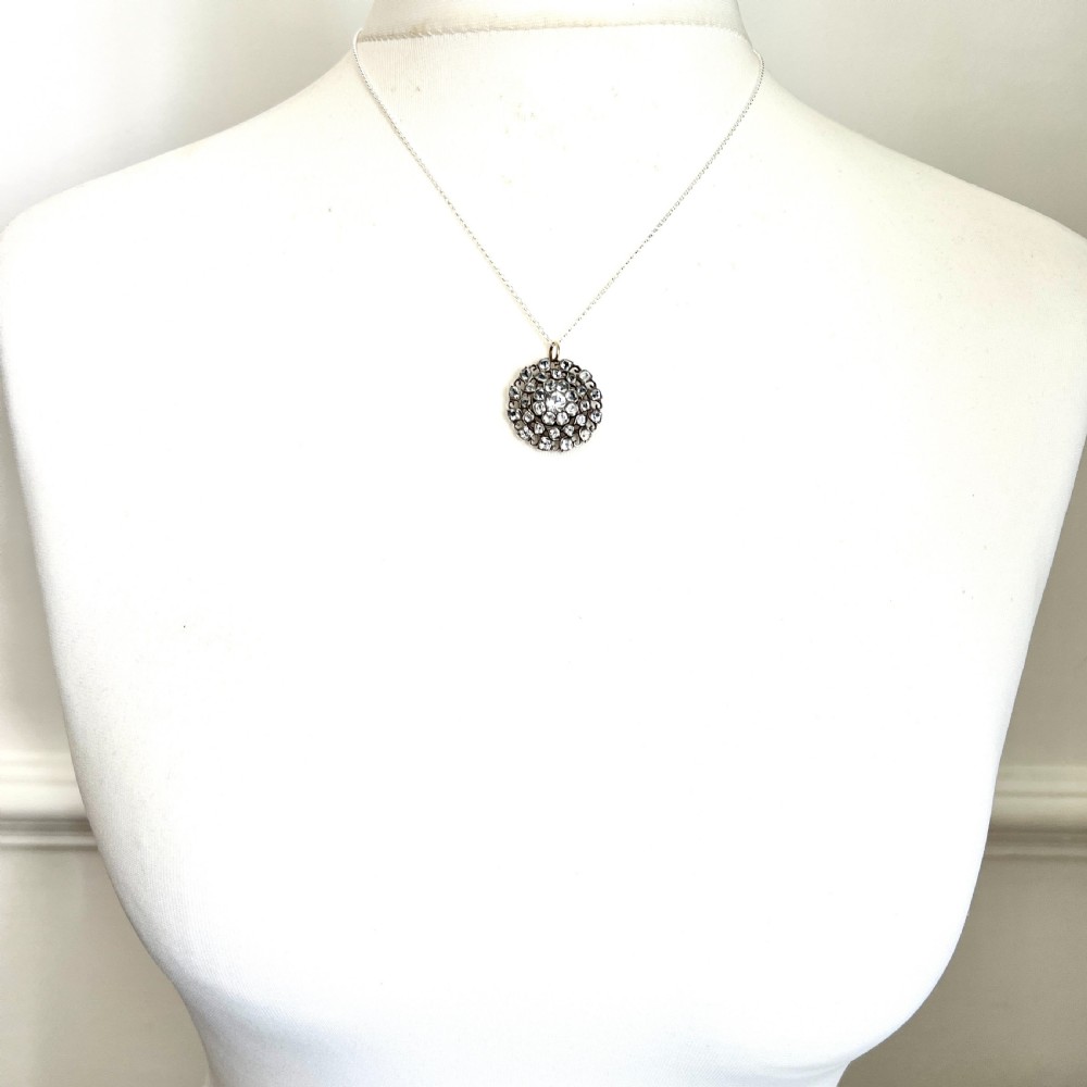 A circular Georgian silver pendant featuring faceted clear paste glass stones with black dot culets arranged in a floral cluster pattern. View VI