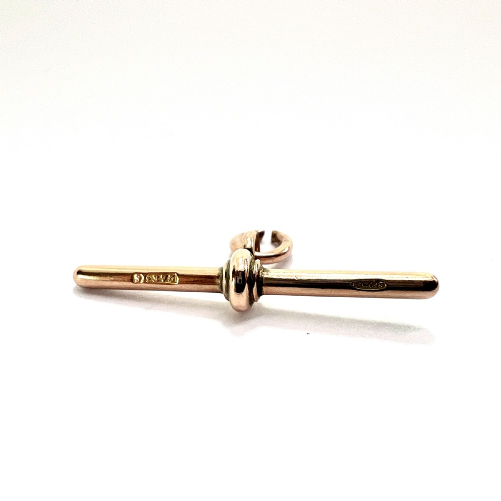 A polished 9ct rose gold Victorian albert T-bar pendant features a central crossbar and an attached jump ring. View IV