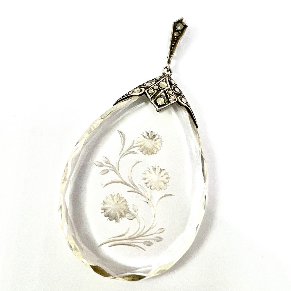 A clear glass teardrop pendant reverse-engraved with a floral motif, topped with a silver decorative cap set with faceted marcasite stones.