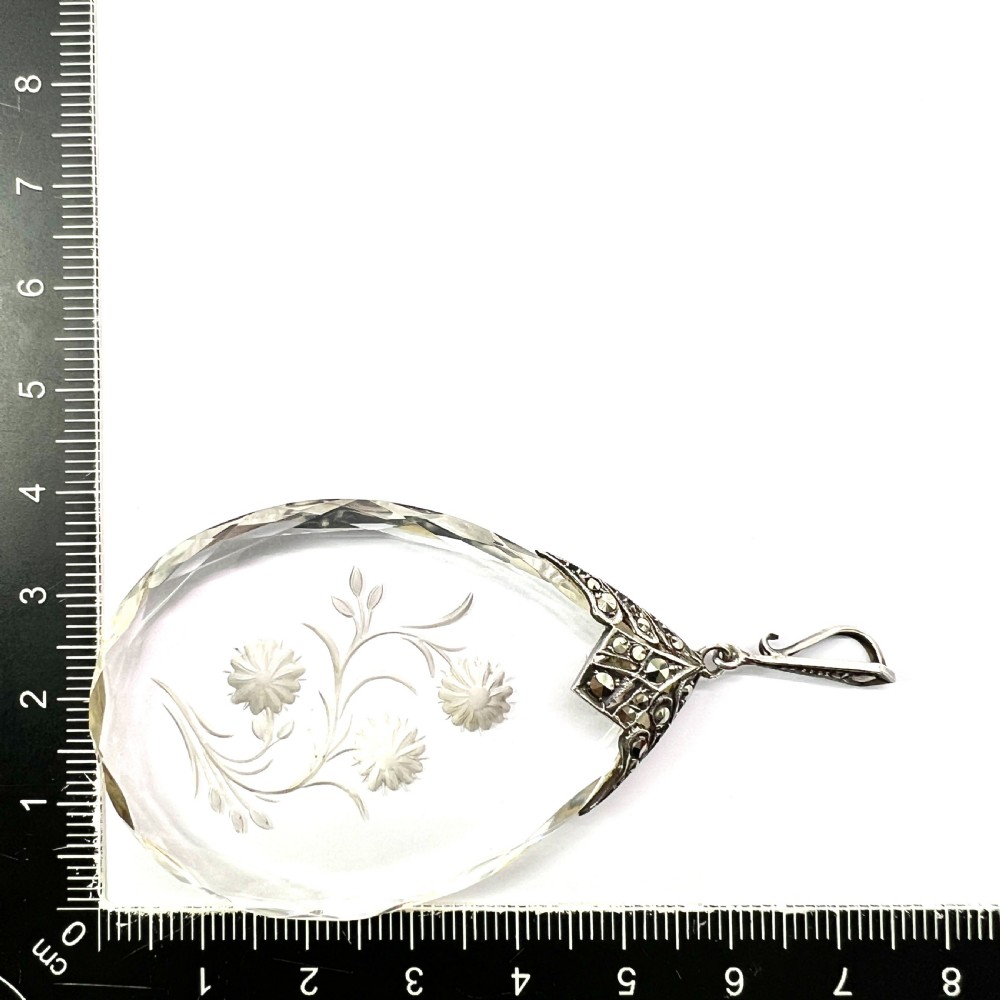 A clear glass teardrop pendant reverse-engraved with a floral motif, topped with a silver decorative cap set with faceted marcasite stones. View VI