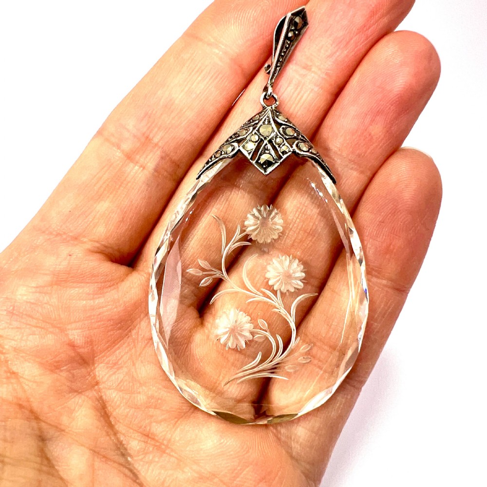 A clear glass teardrop pendant reverse-engraved with a floral motif, topped with a silver decorative cap set with faceted marcasite stones. View VII