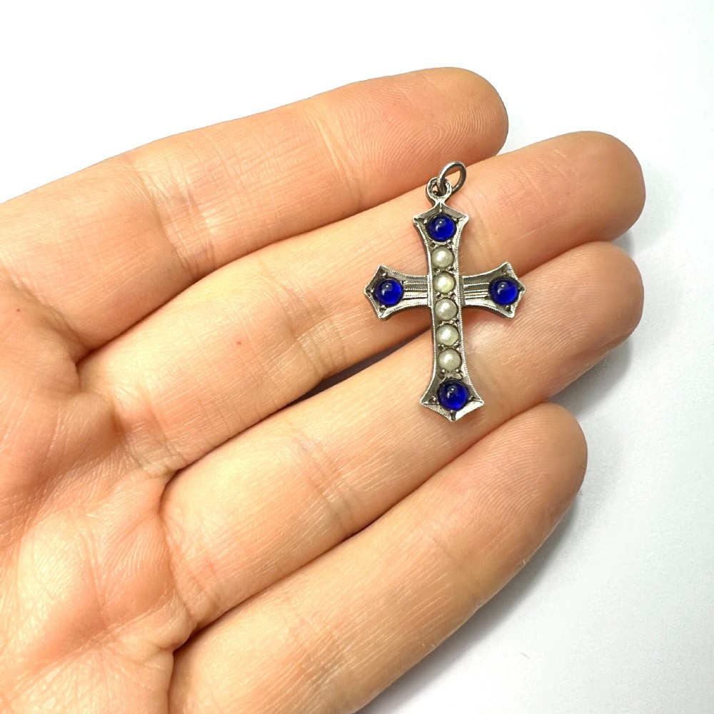 An antique sterling silver cross pendant set with blue paste cabochons and central white pearls against a white background. View VI