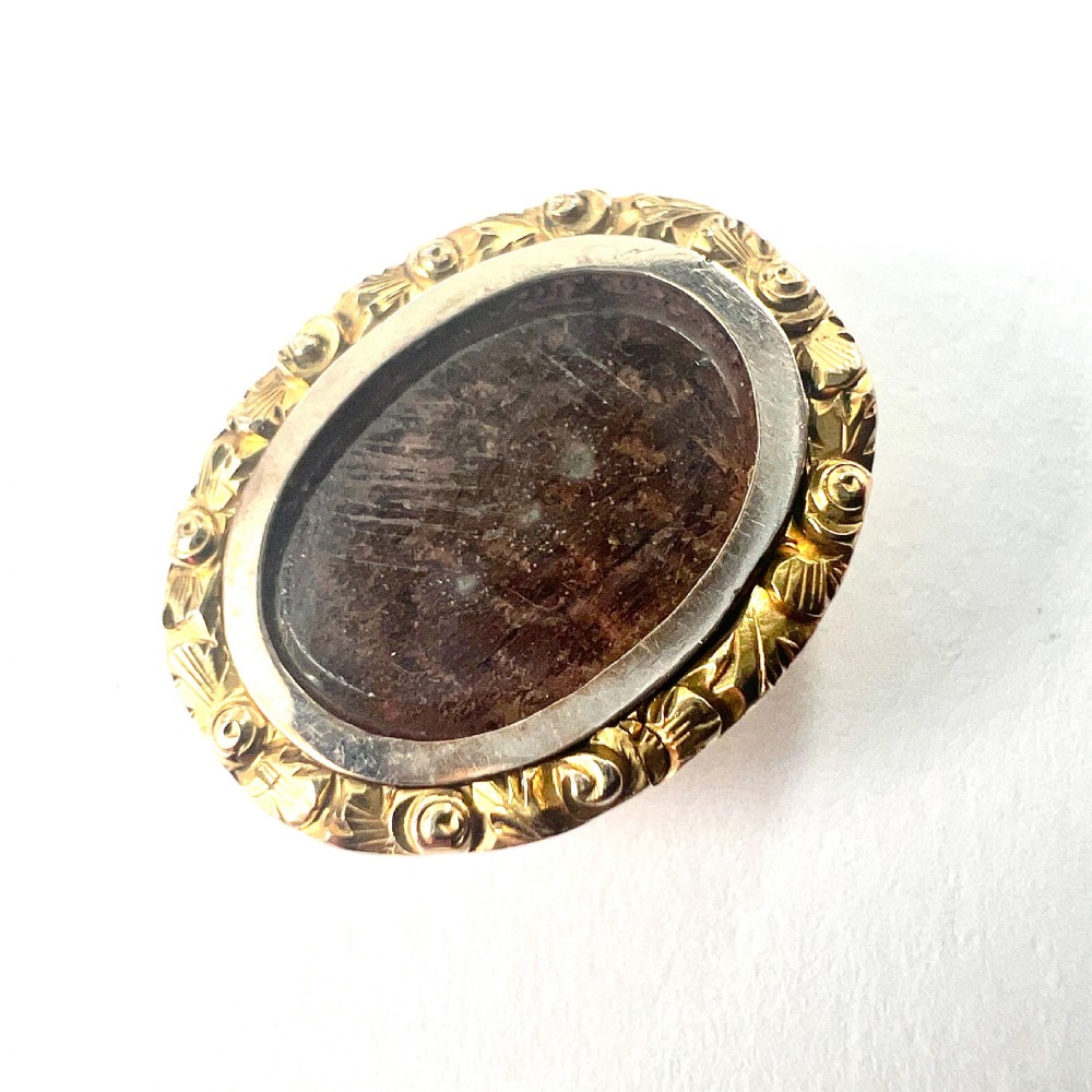 An oval Georgian gold brooch with a chased scroll border surrounding a glass compartment containing brown woven hair.