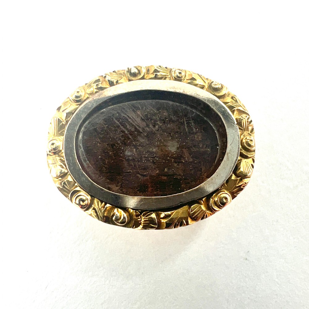 An oval Georgian gold brooch with a chased scroll border surrounding a glass compartment containing brown woven hair. View II