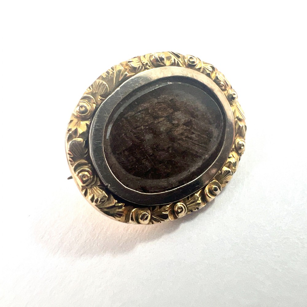 An oval Georgian gold brooch with a chased scroll border surrounding a glass compartment containing brown woven hair. View III