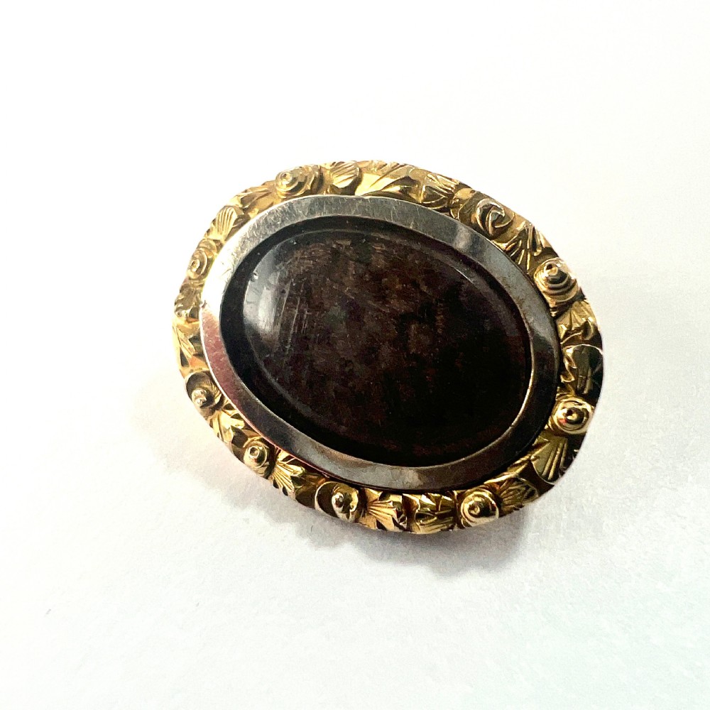 An oval Georgian gold brooch with a chased scroll border surrounding a glass compartment containing brown woven hair. View IV