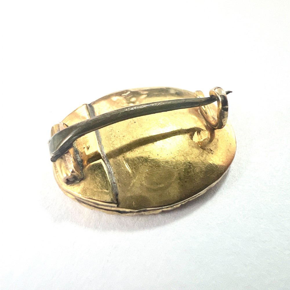 An oval Georgian gold brooch with a chased scroll border surrounding a glass compartment containing brown woven hair. View V
