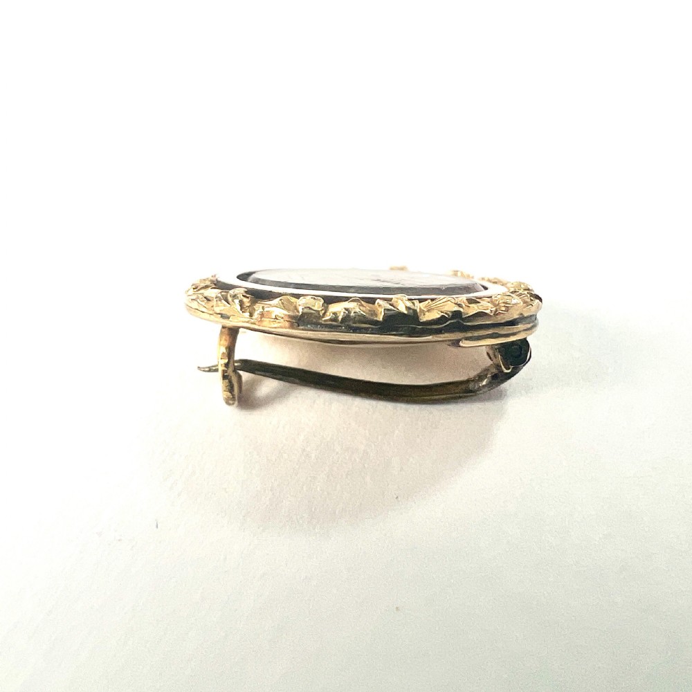 An oval Georgian gold brooch with a chased scroll border surrounding a glass compartment containing brown woven hair. View VI