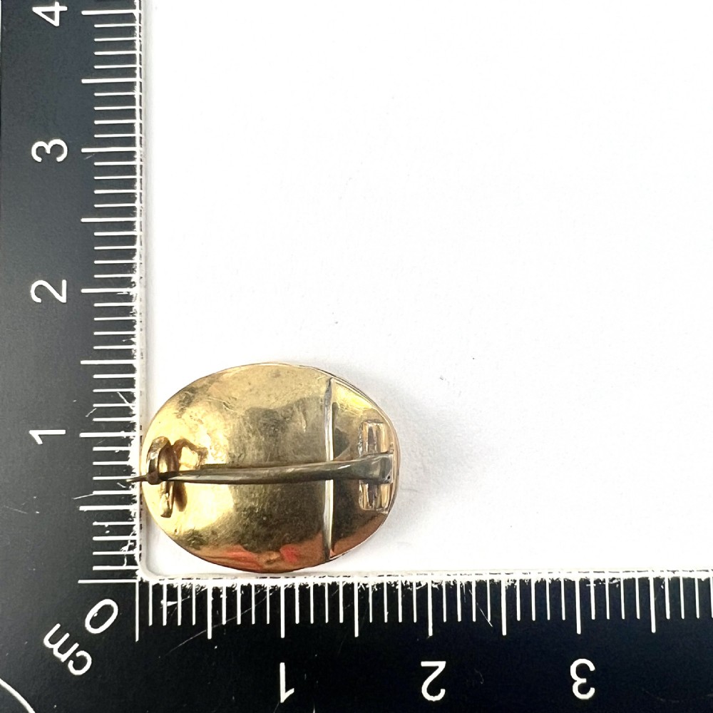 An oval Georgian gold brooch with a chased scroll border surrounding a glass compartment containing brown woven hair. View VII
