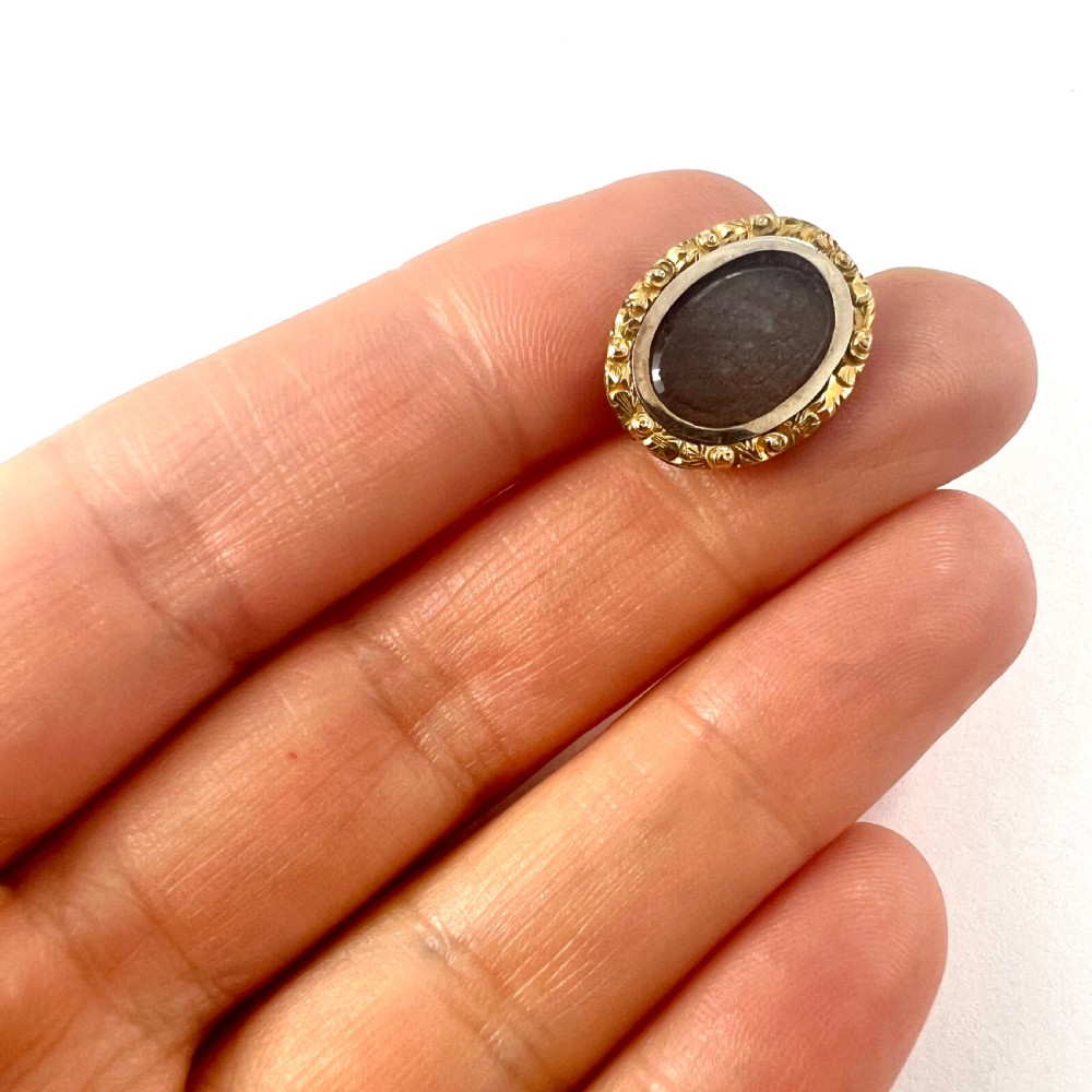 An oval Georgian gold brooch with a chased scroll border surrounding a glass compartment containing brown woven hair. View VIII