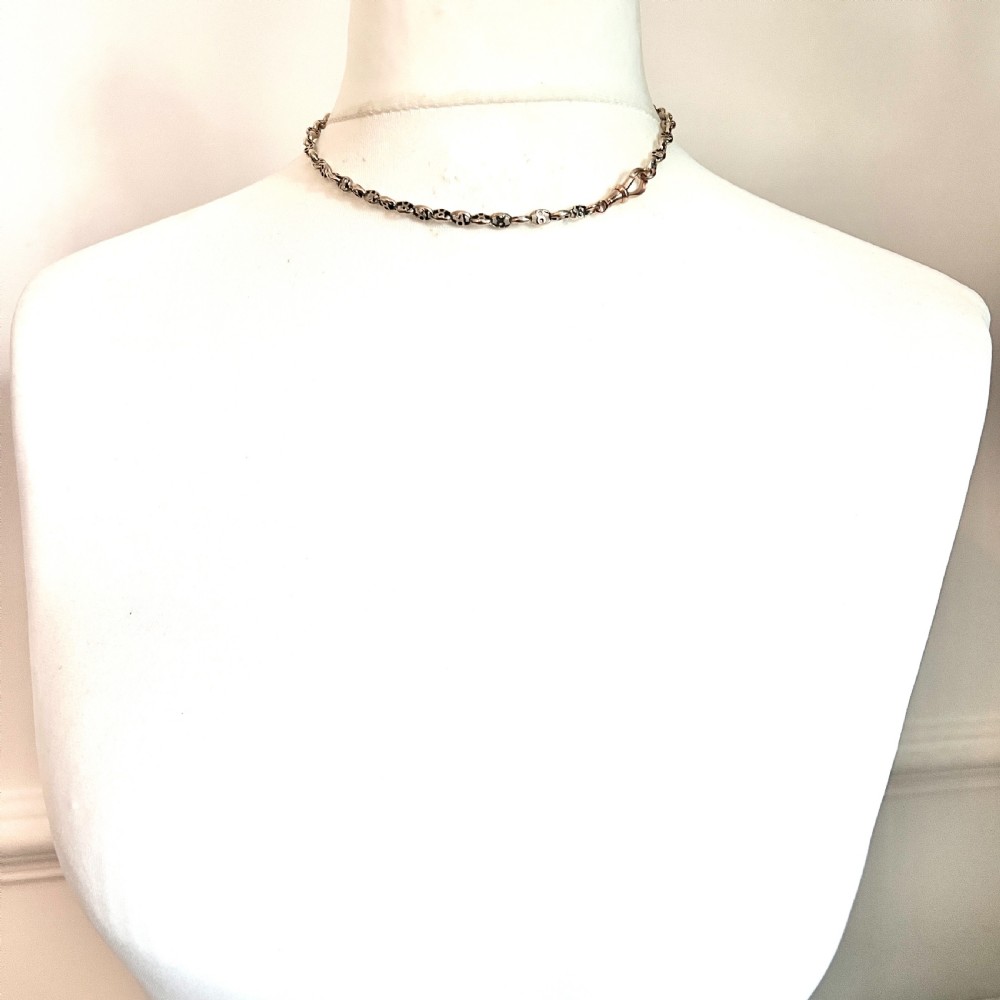 A coiled 9ct yellow gold Victorian fancy link albert chain featuring patterned open links and an attached swivel clip. View IX