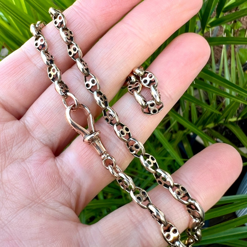 A coiled 9ct yellow gold Victorian fancy link albert chain featuring patterned open links and an attached swivel clip. View X