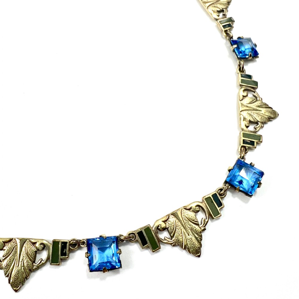 An art deco rolled gold necklace featuring square blue paste stones, leaf motifs, and dark enamel accents on a white background. View III