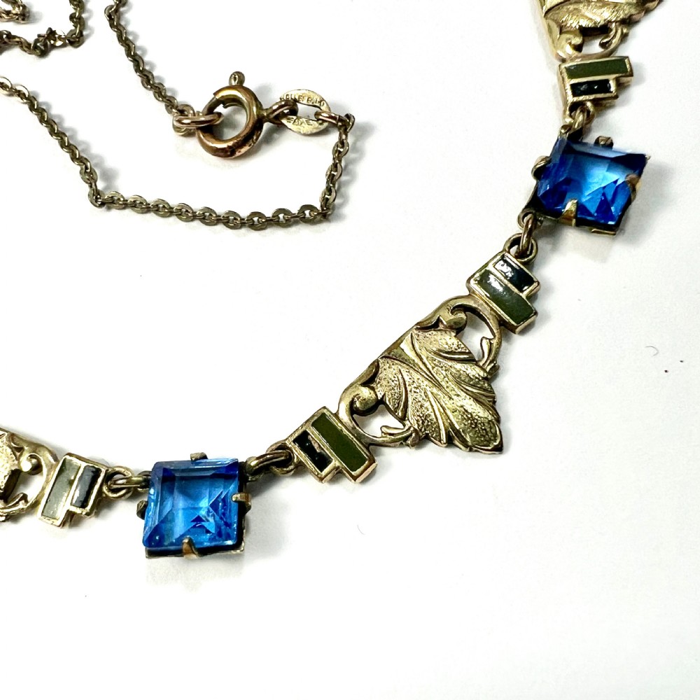 An art deco rolled gold necklace featuring square blue paste stones, leaf motifs, and dark enamel accents on a white background. View IV
