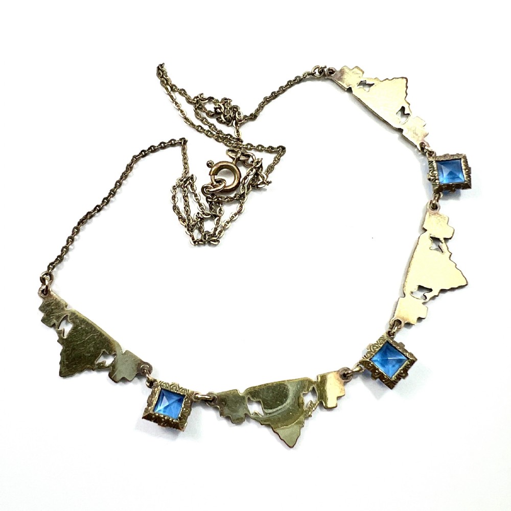 An art deco rolled gold necklace featuring square blue paste stones, leaf motifs, and dark enamel accents on a white background. View V