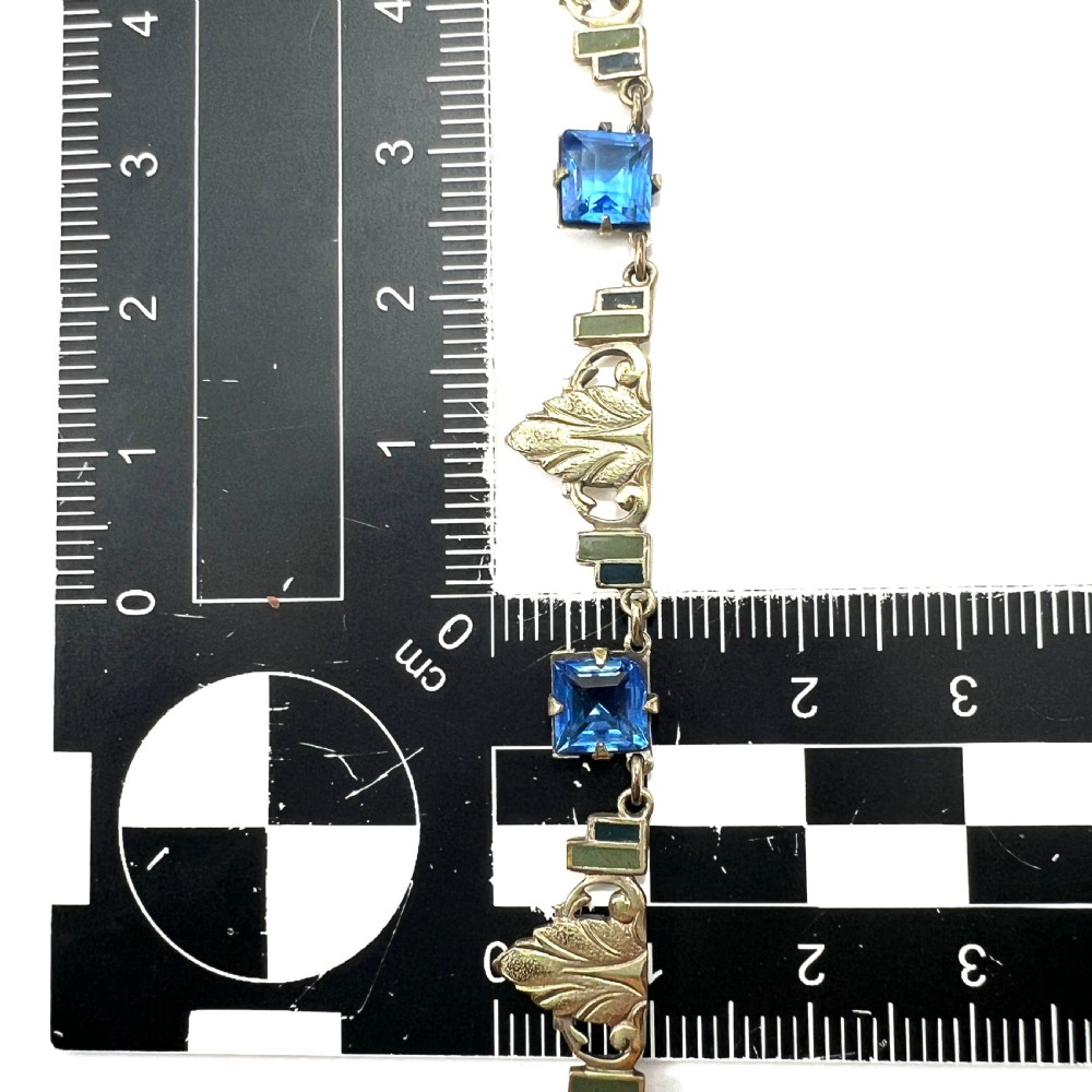 An art deco rolled gold necklace featuring square blue paste stones, leaf motifs, and dark enamel accents on a white background. View VII