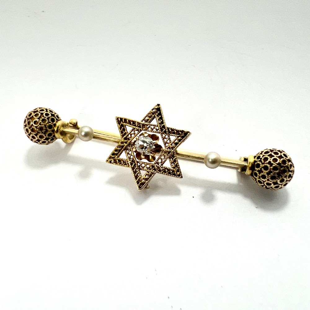 An 18ct yellow gold bar brooch featuring a central filigree Star of David set with a diamond, flanked by two pearls and spherical openwork end beads.