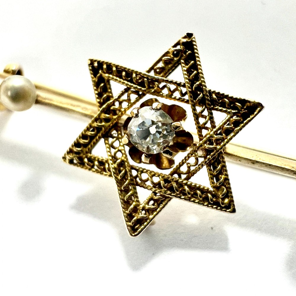 An 18ct yellow gold bar brooch featuring a central filigree Star of David set with a diamond, flanked by two pearls and spherical openwork end beads. View V