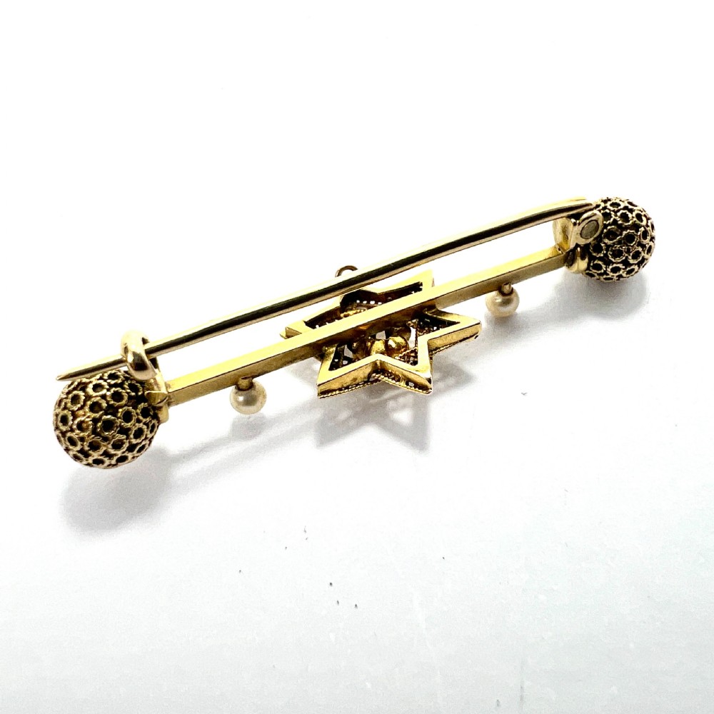 An 18ct yellow gold bar brooch featuring a central filigree Star of David set with a diamond, flanked by two pearls and spherical openwork end beads. View VI