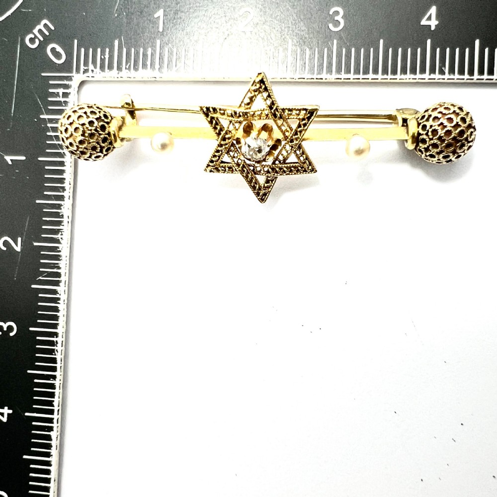 An 18ct yellow gold bar brooch featuring a central filigree Star of David set with a diamond, flanked by two pearls and spherical openwork end beads. View VII
